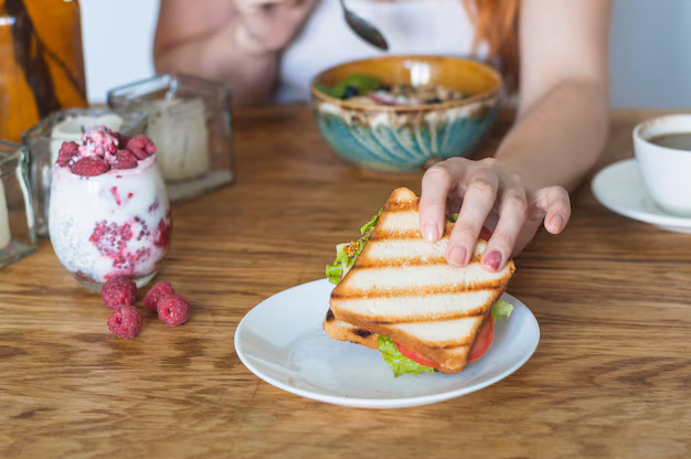 Free photo woman's hand holding sandwich from white plate on wooden table